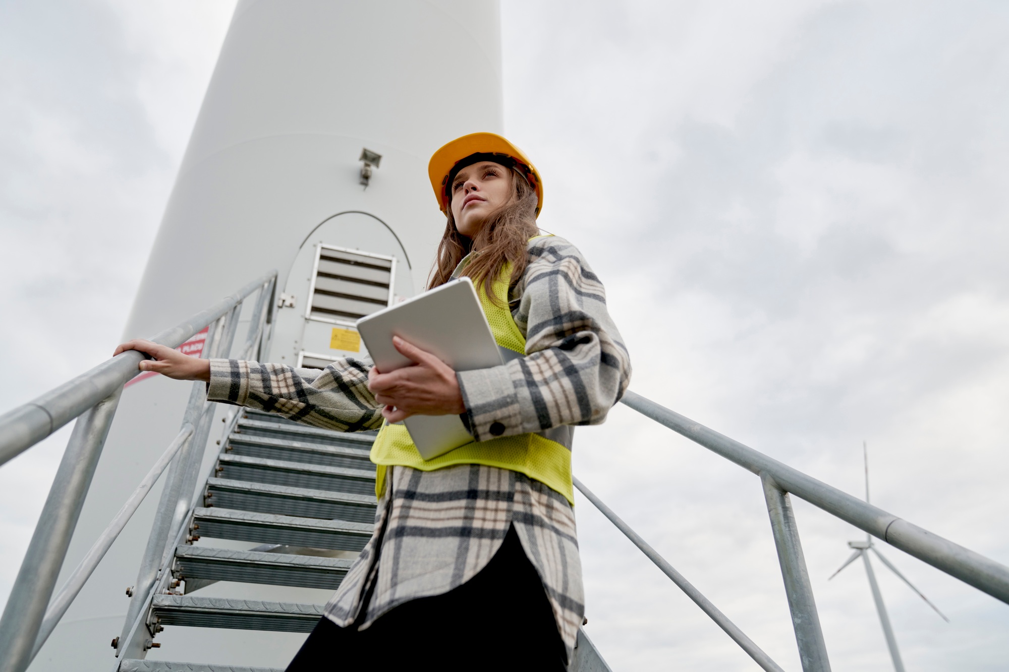 Caucasian female engineer standing next to wind turbine field with digital tablet